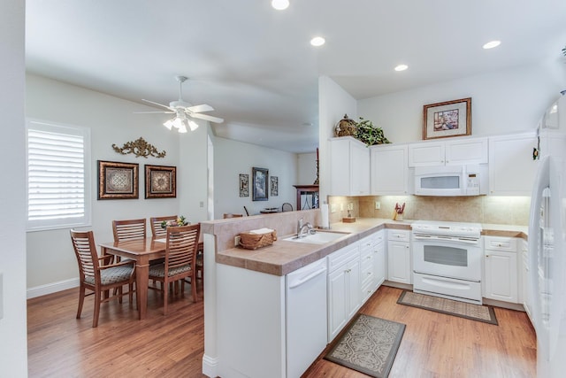 kitchen with white appliances, a sink, a peninsula, light wood-style flooring, and recessed lighting