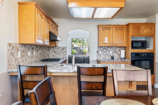 6371 N Babigian Ave, Fresno, CA 93722 - kitchen with black appliances, under cabinet range hood, a sink, a peninsula, and decorative backsplash