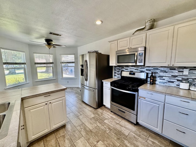 1079 E El Paso Ave, Fresno, CA 93720 - kitchen featuring appliances with stainless steel finishes, a textured ceiling, a ceiling fan, tasteful backsplash, and wood finish floors