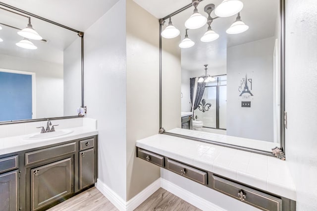 6211 N Cleo Ave, Fresno, CA 93722 - bathroom featuring wood finished floors, vanity, toilet, baseboards, and a chandelier