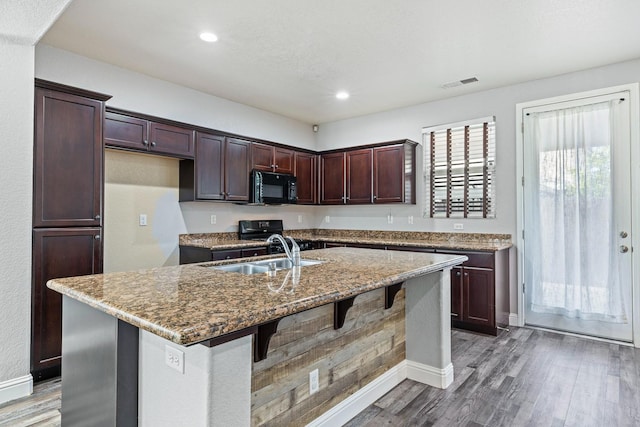 kitchen with black microwave, a sink, wood finished floors, a breakfast bar area, and stone counters