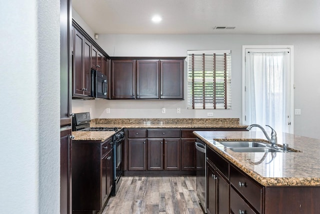 kitchen featuring black appliances, a sink, light wood-type flooring, dark brown cabinetry, and an island with sink