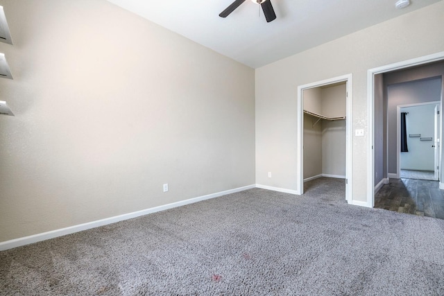 unfurnished bedroom featuring dark carpet, baseboards, a spacious closet, and ceiling fan