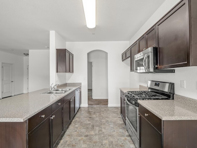 1585 Dallas St, Dinuba, CA 93618 - kitchen featuring appliances with stainless steel finishes, a sink, arched walkways, dark brown cabinetry, and a peninsula