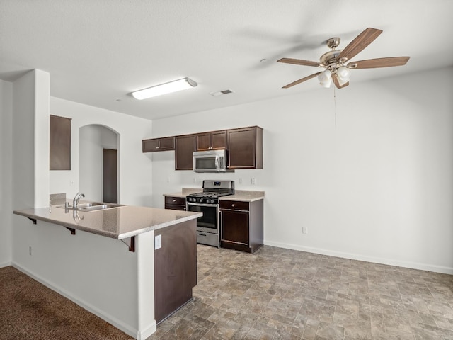 1585 Dallas St, Dinuba, CA 93618 - kitchen with appliances with stainless steel finishes, a sink, arched walkways, a breakfast bar, and dark brown cabinets