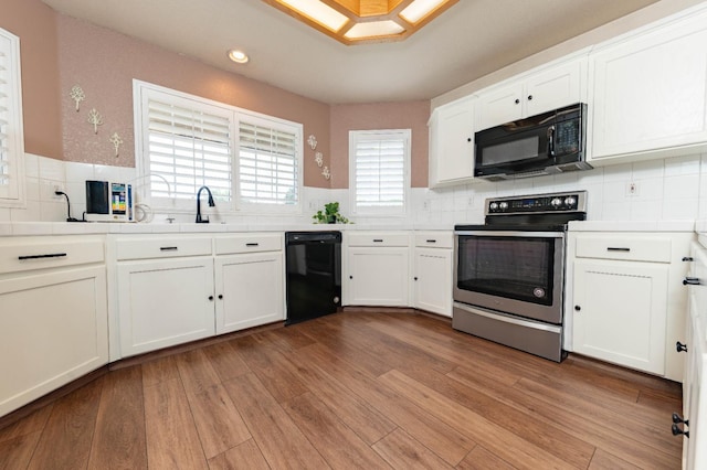 kitchen with black appliances, white cabinetry, a sink, decorative backsplash, and light wood-style flooring