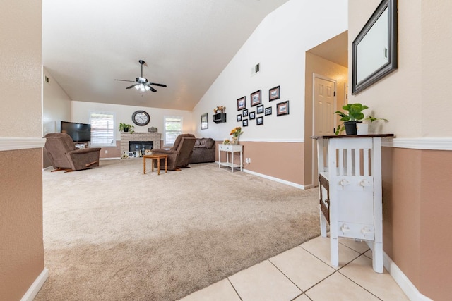 living area with ceiling fan, light colored carpet, a fireplace, baseboards, and high vaulted ceiling