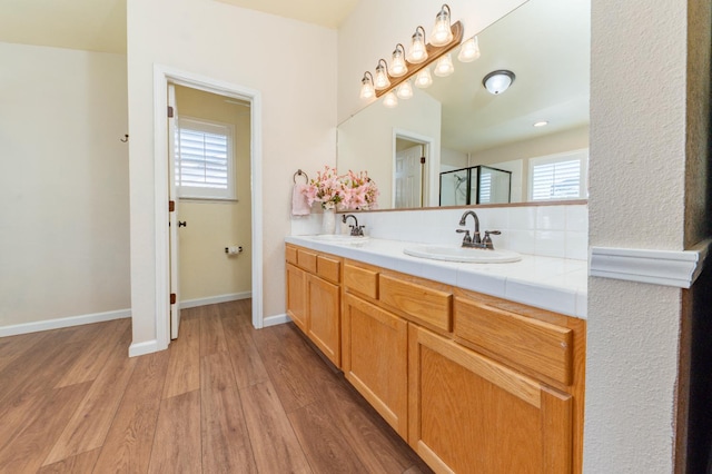 full bath featuring wood finished floors, a shower stall, double vanity, and baseboards