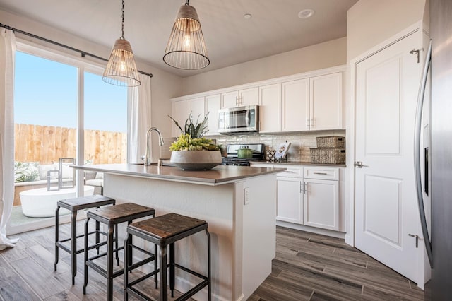 1161 Maclure Ave W, Madera, CA 93636 - kitchen with appliances with stainless steel finishes, white cabinets, decorative backsplash, a kitchen island with sink, and a sink