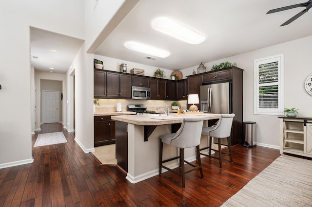 3942 Harlan Ranch Blvd, Clovis, CA 93619 - kitchen with appliances with stainless steel finishes, dark brown cabinetry, light countertops, a breakfast bar area, and dark wood-style floors