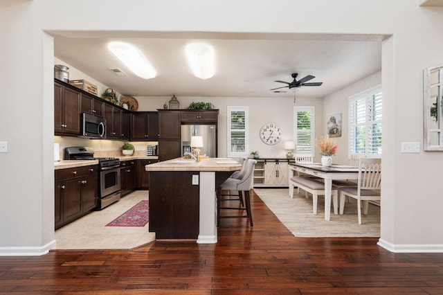 3942 Harlan Ranch Blvd, Clovis, CA 93619 - kitchen featuring stainless steel appliances, dark brown cabinetry, light wood finished floors, and a breakfast bar area