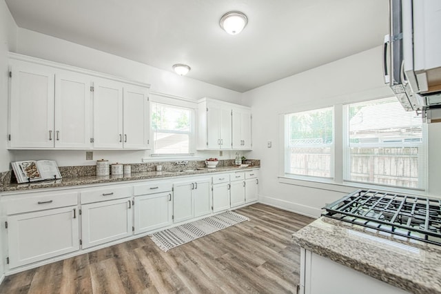 1010 N Ferger Ave, Fresno, CA 93728 - kitchen with white cabinets, light wood finished floors, light stone counters, a sink, and baseboards