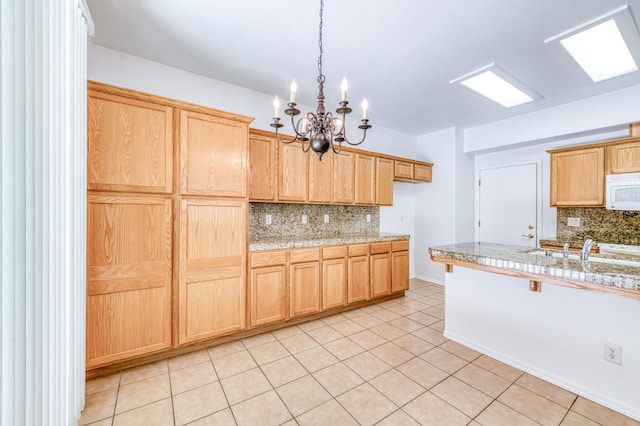 83 W Bohemia Ln, Clovis, CA 93619 - kitchen with white microwave, decorative backsplash, a chandelier, light brown cabinetry, and a sink