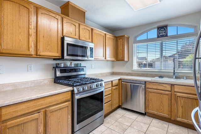 kitchen with appliances with stainless steel finishes, light tile patterned flooring, light countertops, and a sink