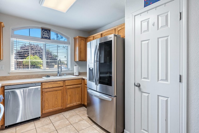 kitchen with stainless steel appliances, a sink, light tile patterned flooring, light countertops, and brown cabinets