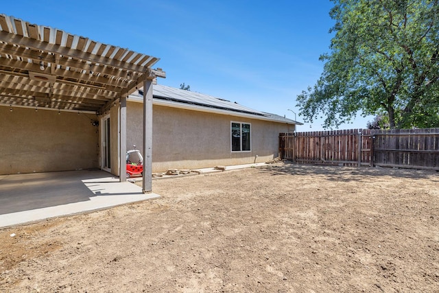 rear view of property featuring stucco siding, solar panels, a patio area, a fenced backyard, and a pergola