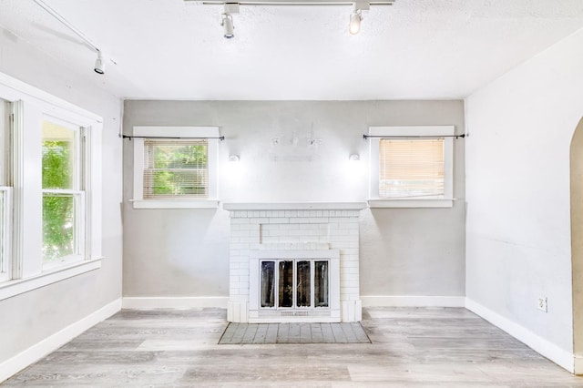 1934 N Vagedes Ave, Fresno, CA 93705 - unfurnished living room featuring rail lighting, a brick fireplace, wood finished floors, arched walkways, and baseboards