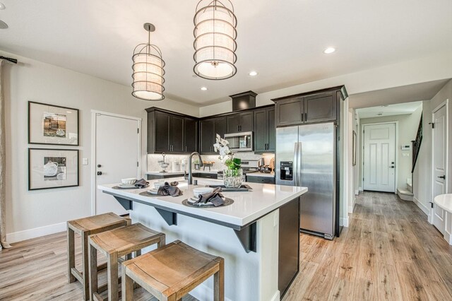1165 Maclure Ave W, Madera, CA 93636 - kitchen with stainless steel appliances, light countertops, baseboards, light wood finished floors, and tasteful backsplash