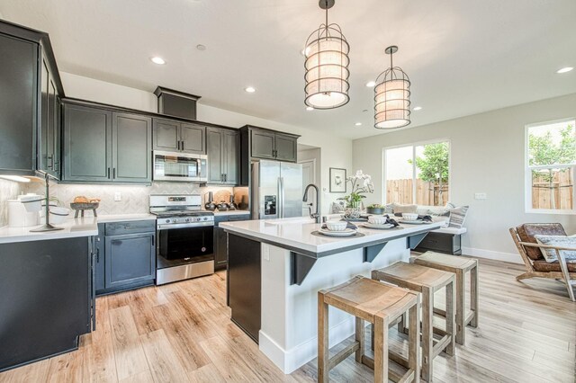 1165 Maclure Ave W, Madera, CA 93636 - kitchen with appliances with stainless steel finishes, light countertops, light wood finished floors, a kitchen breakfast bar, and recessed lighting