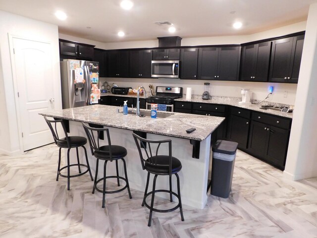 865 S Bridle Ave, Fresno, CA 93727 - kitchen featuring appliances with stainless steel finishes, dark cabinets, an island with sink, light stone countertops, and recessed lighting
