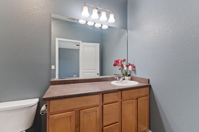 bathroom with a textured wall, vanity, and toilet