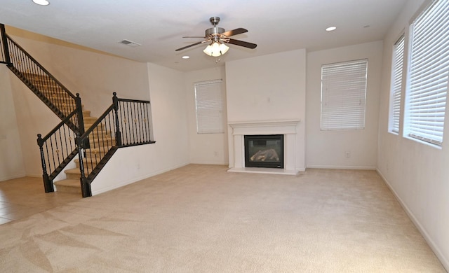 unfurnished living room featuring carpet, a glass covered fireplace, recessed lighting, a ceiling fan, and stairway