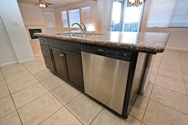 kitchen featuring stainless steel dishwasher, a sink, light tile patterned floors, and dark stone counters