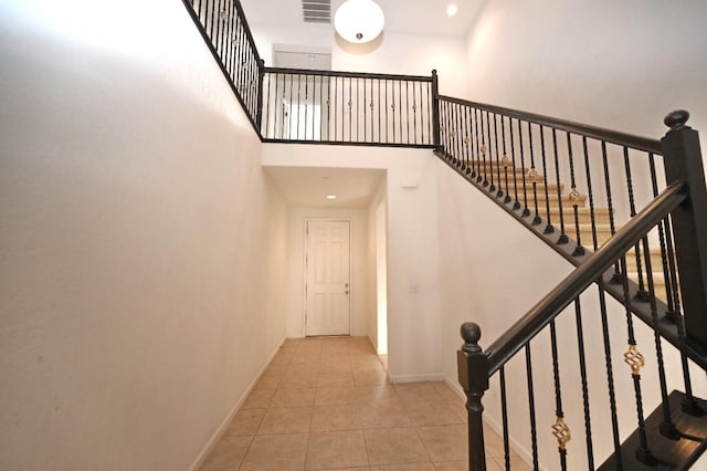 stairs with tile patterned floors, baseboards, and a high ceiling