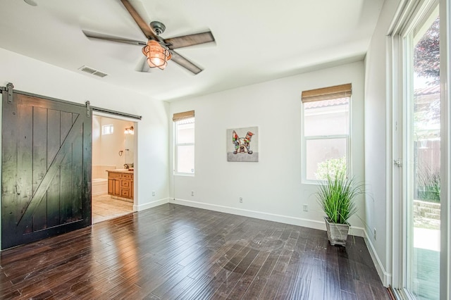 unfurnished bedroom featuring a barn door, dark wood-type flooring, connected bathroom, and baseboards