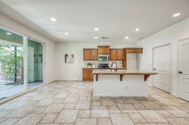 kitchen with stainless steel appliances, brown cabinetry, baseboards, light stone countertops, and recessed lighting