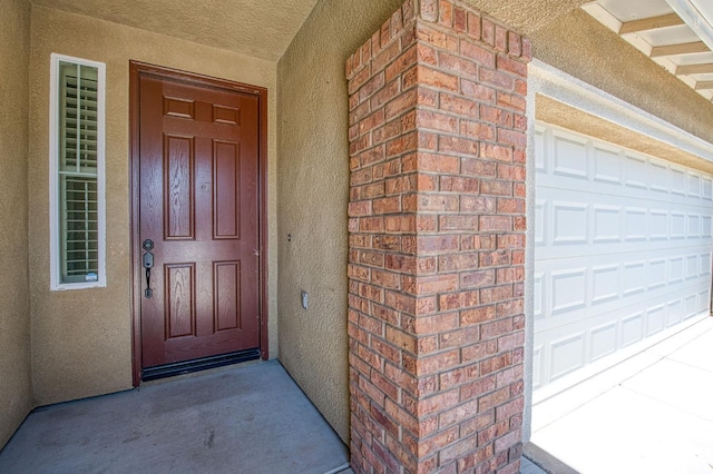 property entrance featuring stucco siding, a garage, and brick siding