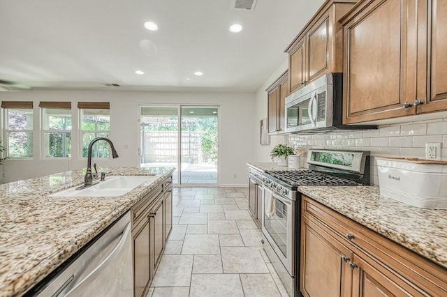 kitchen featuring stainless steel appliances, a sink, recessed lighting, decorative backsplash, and brown cabinetry
