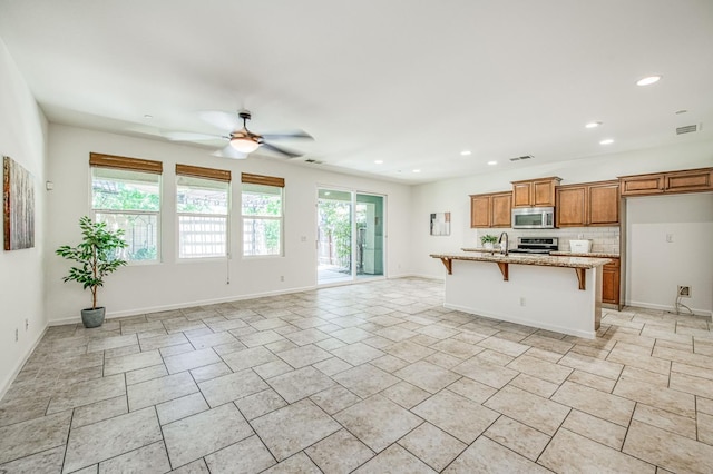 kitchen with stainless steel appliances, ceiling fan, brown cabinetry, a kitchen breakfast bar, and recessed lighting