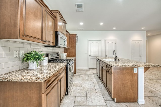 kitchen featuring appliances with stainless steel finishes, a sink, backsplash, brown cabinets, and recessed lighting