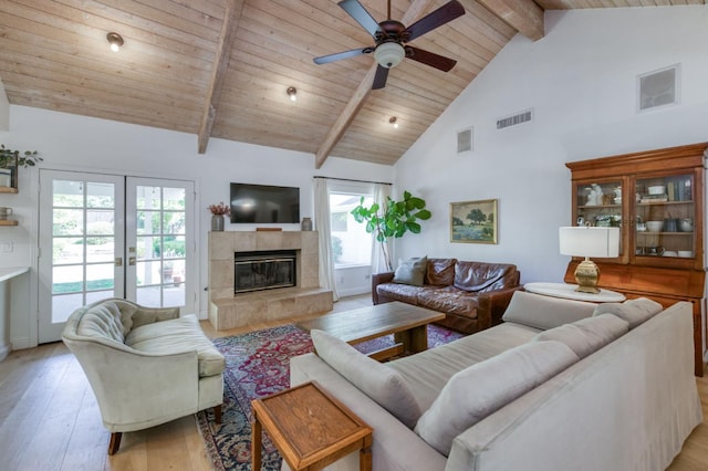 living room with light wood-style floors, high vaulted ceiling, a ceiling fan, a tiled fireplace, and wooden ceiling with exposed beams