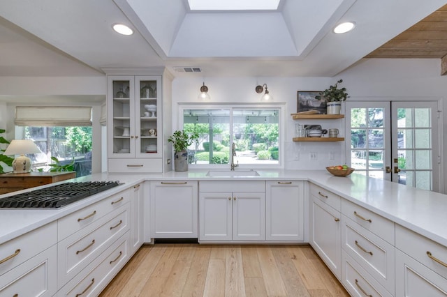 kitchen featuring a sink, gas cooktop, light countertops, white cabinets, and recessed lighting