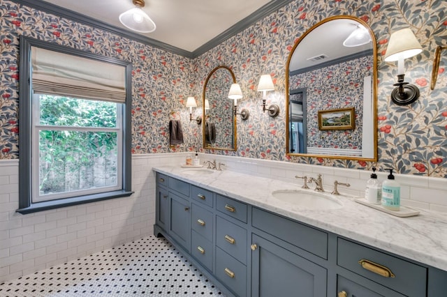 bathroom featuring crown molding, wainscoting, double vanity, and wallpapered walls