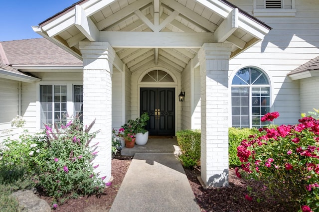 entrance to property featuring a shingled roof and brick siding