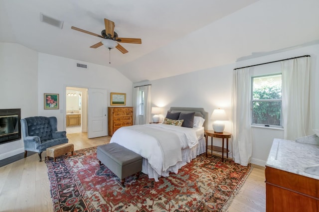 bedroom featuring vaulted ceiling, light wood-style flooring, connected bathroom, a ceiling fan, and baseboards
