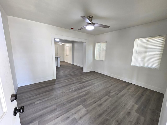 spare room featuring a ceiling fan, dark wood-type flooring, and baseboards