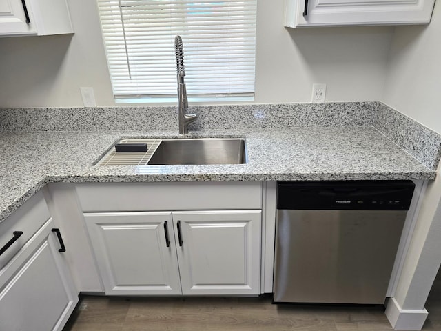 kitchen featuring stainless steel dishwasher, a sink, white cabinetry, wood finished floors, and light stone counters