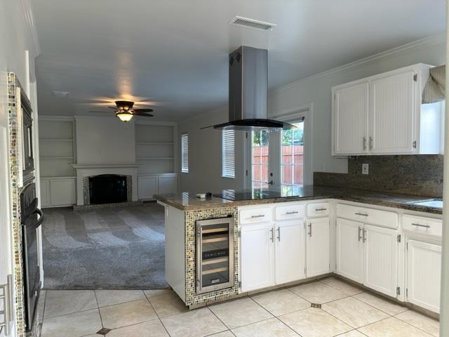 10752 N Windham Bay Cir, Fresno, CA 93730 - kitchen featuring beverage cooler, island range hood, a ceiling fan, a peninsula, and a fireplace with raised hearth
