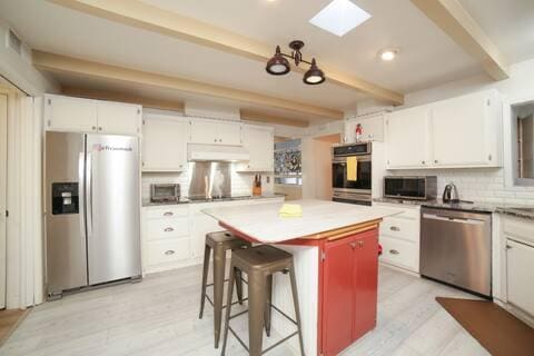 5543 N 7th St, Fresno, CA 93710 - kitchen with stainless steel appliances, beamed ceiling, under cabinet range hood, backsplash, and white cabinetry