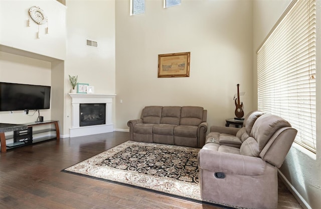 7026 E Dayton Ave, Fresno, CA 93737 - living room featuring dark wood-style flooring, a towering ceiling, plenty of natural light, baseboards, and a glass covered fireplace