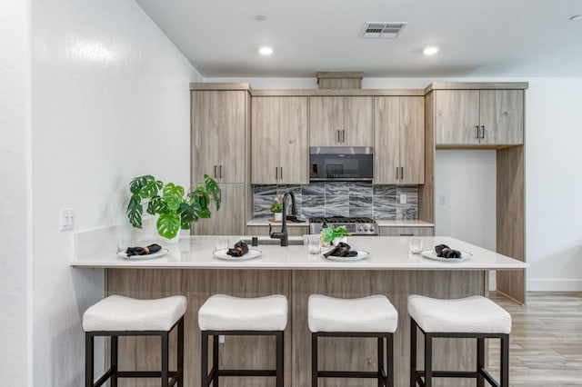 2867 E Tamarind Dr, Fresno, CA 93730 - kitchen featuring stainless steel microwave, a peninsula, light brown cabinets, a breakfast bar, and recessed lighting