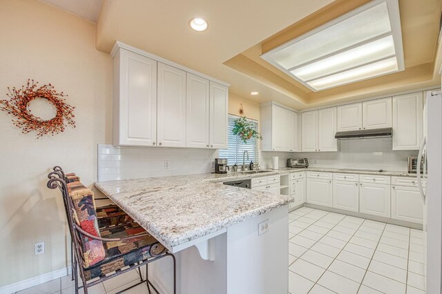 2895 W Kensington Ln, Fresno, CA 93711 - kitchen featuring a tray ceiling, a peninsula, white cabinetry, under cabinet range hood, and decorative backsplash