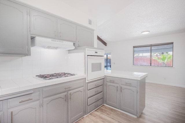 1617 W Indianapolis Ave, Fresno, CA 93705 - kitchen with under cabinet range hood, white appliances, a peninsula, tile countertops, and light wood-style floors