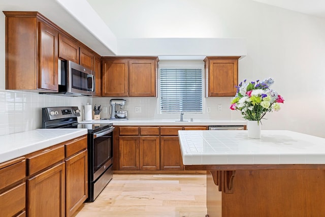 2871 E Ryan Ln, Fresno, CA 93720 - kitchen featuring stainless steel appliances, light wood-type flooring, backsplash, and brown cabinetry