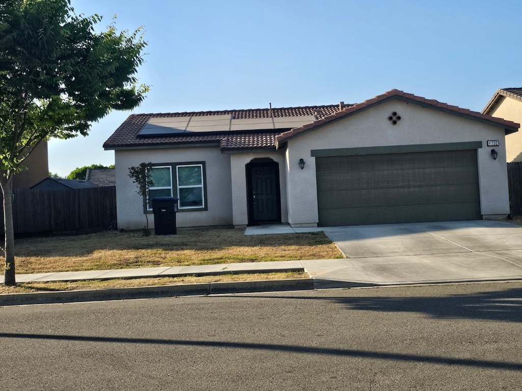 4232 E Harold Ave, Visalia, CA 93292 - mediterranean / spanish home featuring stucco siding, roof mounted solar panels, a tiled roof, and an attached garage