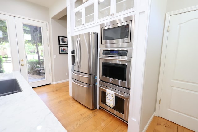2143 Everglade Ave, Clovis, CA 93619 - kitchen with appliances with stainless steel finishes, light wood finished floors, white cabinetry, glass insert cabinets, and baseboards